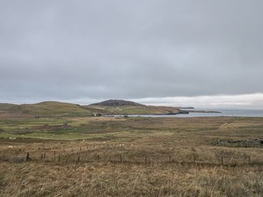A rural landscape with grassy fields, sheep, scattered houses, hills, and a body of water at Garraidh Ghorm Pod in Conista
