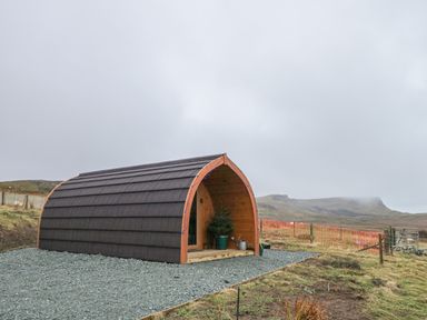 A small wooden pod with dark roof shingles on a gravel base in a rural area at Garraidh Ghorm Pod in Conista