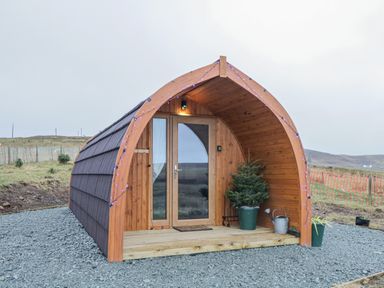 A small wooden pod with curved roof a glass door potted plants and a watering can at Garraidh Ghorm Pod in Conista