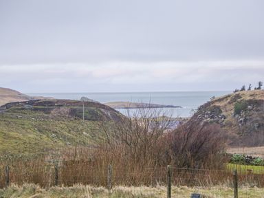 A coastal landscape with grassy hills and ocean in the background at Garraidh Ghorm Pod in Conista