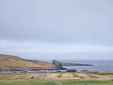 A rural coastal landscape with fields sheep a few buildings a rocky hill and the sea at Garraidh Ghorm Pod in Conista