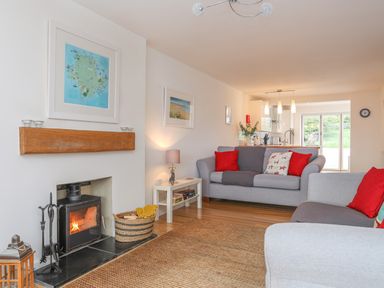 A living room with a fireplace two grey sofas with red cushions a small white table and kitchen in the background at Sisial-Y-Mor in Rhosneigr