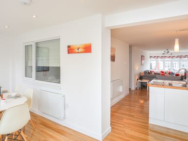 A dining area with chairs and a table next to a kitchen with a sink and a living room with sofas and cushions at Sisial-Y-Mor in Rhosneigr