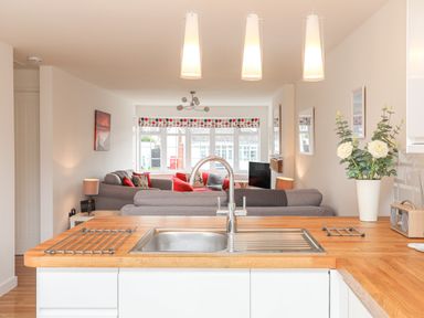 A kitchen sink with a wooden countertop and a view of a living room with grey sofas and red cushions at Sisial-Y-Mor in Rhosneigr