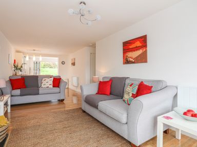 A living room with two gray sofas red cushions and a white side table with a bowl of apples at Sisial-Y-Mor in Rhosneigr