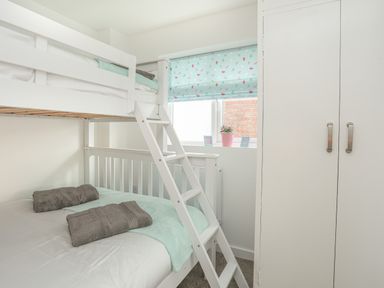 A bedroom with a white bunk bed towels on the lower bed a window with a blue patterned blind and a white wardrobe at Sisial-Y-Mor in Rhosneigr