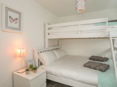 A bedroom with a white bunk bed white bedside table with plants and lamp and a framed butterfly picture on the wall at Sisial-Y-Mor in Rhosneigr