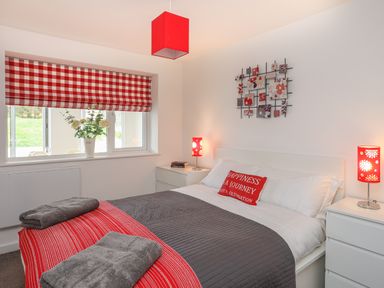 A bedroom with a double bed two bedside tables with lamps and a window with a red checkered blind at Sisial-Y-Mor in Rhosneigr