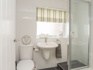 A bathroom with a toilet a sink a towel ring with a towel a glass shower enclosure and a window with a striped blind at Sisial-Y-Mor in Rhosneigr