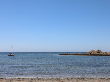 A beach with a small sailboat on the water and rocky outcrop in the distance at Sisial-Y-Mor in Rhosneigr