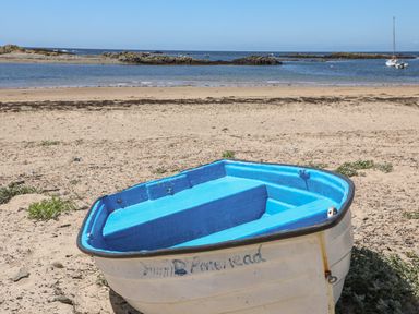 A small empty boat on a sandy beach with rocks and water in the background at Sisial-Y-Mor in Rhosneigr