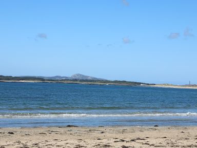 A sandy beach with small waves and a body of water with land and hills in the distance at Sisial-Y-Mor in Rhosneigr