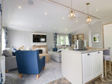 An open living room with sofas a blue armchair a wall mounted TV and a kitchen island at Pinehurst Lodge in St Day