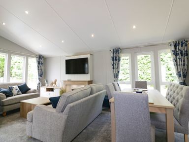 A living room with sofas a television and a dining table by windows at Pinehurst Lodge in St Day