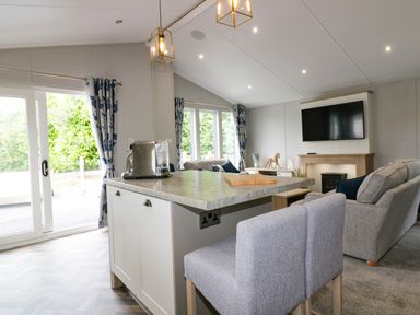 An open living room with a kitchen island chairs sofa TV and fireplace at Pinehurst Lodge in St Day