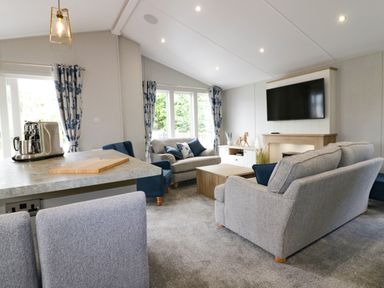 A living room with sofas a television mounted above a fireplace and curtains at Pinehurst Lodge in St Day