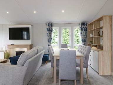 A dining table with six chairs in a room with a sofa a TV on the wall and a wooden cabinet at Pinehurst Lodge in St Day