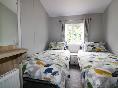 A bedroom with two single beds a window and a bedside table at Pinehurst Lodge in St Day