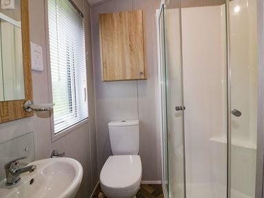 A bathroom with a sink toilet shower window and a wooden cabinet at Pinehurst Lodge in St Day