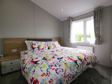 A bedroom with a bed with floral bedding and a window with curtains at Pinehurst Lodge in St Day