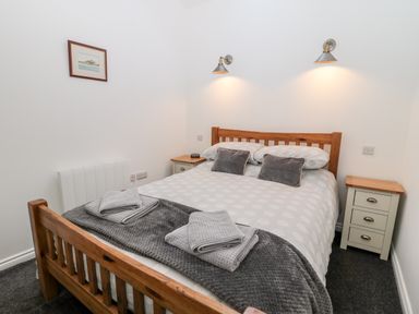 A bedroom with a wooden bed frame bedside tables and wall lights at The Old Stables in Belford