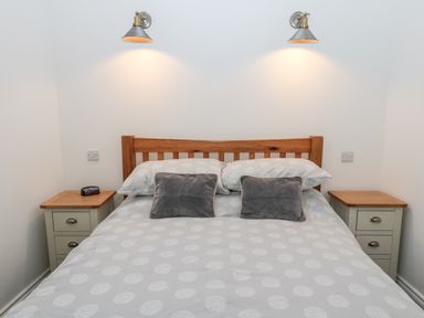 A bedroom with a wooden bed frame two grey pillows and matching bedside tables with lamps at The Old Stables in Belford