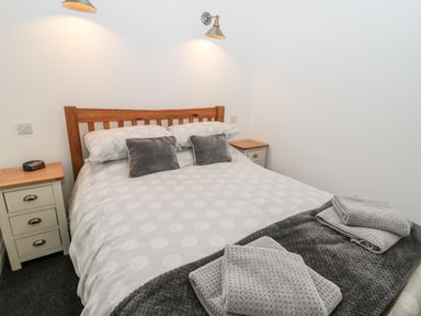 A bedroom with a wooden bed and bedside tables with lamps on the walls at The Old Stables in Belford