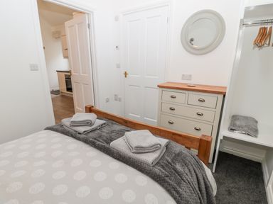 A bedroom with a wooden bed, folded towels on the bed, a chest of drawers, a round mirror, and an open closet at The Old Stables in Belford