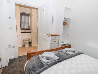 A bedroom with a wooden bed frame and folded towels on the bed facing an open door to a bathroom with a toilet and a window at The Old Stables in Belford