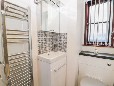 A bathroom with a white sink, wall-mounted chrome towel rail, tiled backsplash, and a window with vertical blinds at The Old Stables in Belford