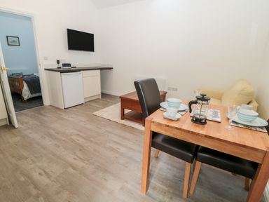 A dining table set for two in a living area with a wall-mounted tv a small fridge a coffee table and a sofa at The Old Stables in Belford