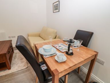A dining table set with plates cups and a coffee press next to a beige sofa and wooden coffee table at The Old Stables in Belford