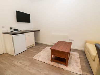 A small living area with a mounted television wooden coffee table beige sofa and mini fridge at The Old Stables in Belford