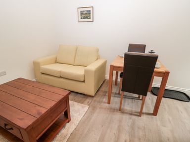 A small room with a beige loveseat sofa a wooden coffee table a dining table with two chairs and a framed picture on the wall at The Old Stables in Belford