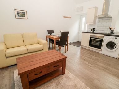 A living area with a beige sofa a wooden coffee table a small dining table with two chairs and a kitchen with appliances at The Old Stables in Belford
