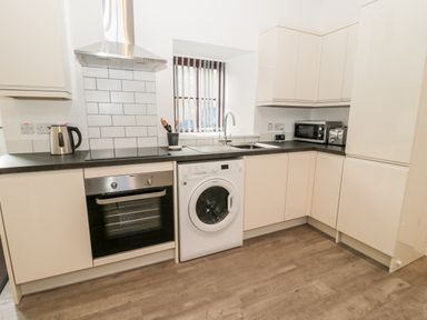 A kitchen with white cabinets appliances a washing machine oven microwave and kettle at The Old Stables in Belford