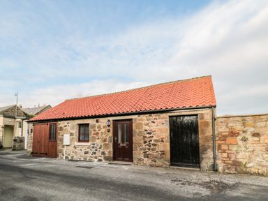 A stone building with red tiled roof and doors on a paved street at The Old Stables in Belford