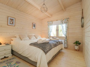 A bedroom with a large bed bedside table framed pictures and a window with patterned curtains at Gardeners Lodge in Huby
