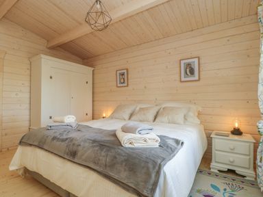 A bedroom with a bed, white wardrobe, nightstand with lamp and framed pictures on walls at Gardeners Lodge in Huby