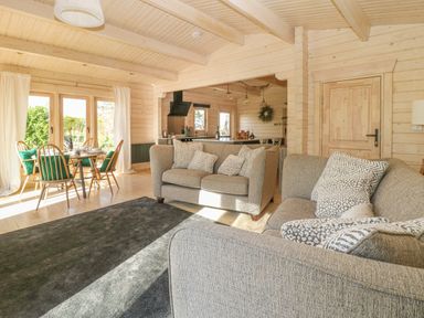 A living room with two grey sofas and patterned cushions next to a dining area with wooden chairs and table at Gardener's Lodge in Huby