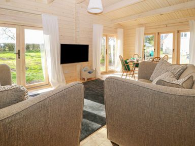 A living room with gray sofas a wall-mounted TV a dining table and chairs near windows at Gardener's Lodge in Huby