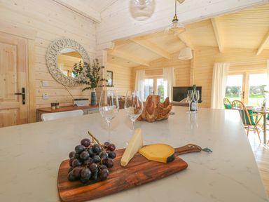 A kitchen island with cheese and grapes a living area with chairs a mirror and a window at Gardener's Lodge in Huby