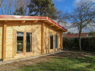 A wooden cabin with glass doors and a green garden at Gardener's Lodge in Huby