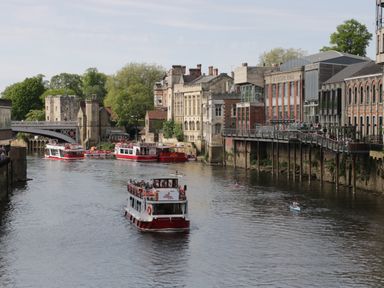 A river with boats and buildings along the banks and a pedestrian bridge over the water at Gardener's Lodge in Huby