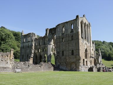 Ruins of a large stone abbey with arches and tall windows on a grassy area surrounded by trees at Gardeners Lodge in Huby