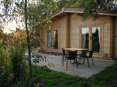 A wooden cabin with glass doors and a patio with table and four chairs surrounded by trees at Gardeners Lodge in Huby
