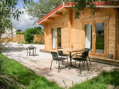 An outdoor patio area with a wooden table and four chairs next to a wooden cabin at Gardener's Lodge in Huby