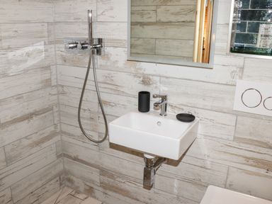 A small white sink with a faucet and two black containers mounted on a tiled wall next to a handheld shower in a bathroom at Gardeners Lodge in Huby