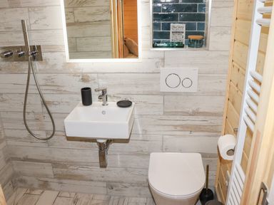 A bathroom with a wall-mounted sink a toilet a shower head and a mirror at Gardener's Lodge in Huby