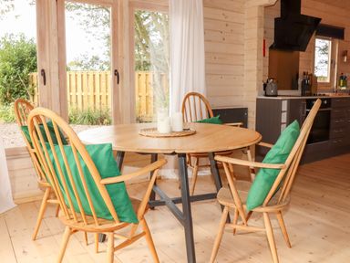 A dining area with a round wooden table and four wooden chairs with green cushions at Gardener's Lodge in Huby